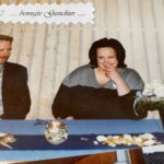 Lachendes Paar am Tisch mit maritimem Dekor und Leuchtturm bei Feierlichkeit.