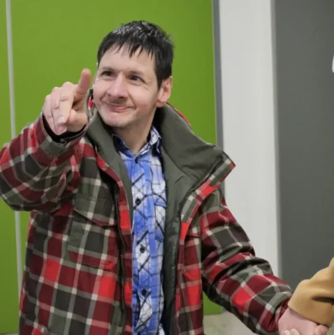 Mann in karierter Winterjacke zeigt nach vorn und hält eine Hand im Innenraum.