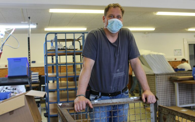 Gruppenleiter Mario Straub in der Lebenshilfe-Werkstatt, steht am Arbeitstisch mit Maske.