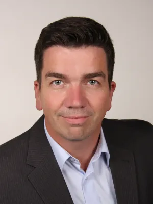 Professionelles Business-Porträt von Michael Thierstein im grauen Anzug und hellblauem Hemd.