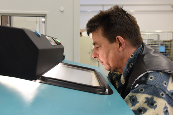 Mitarbeiter prüft Werkstück an Sandstrahlanlage im Industriebetrieb durch Sichtfenster.