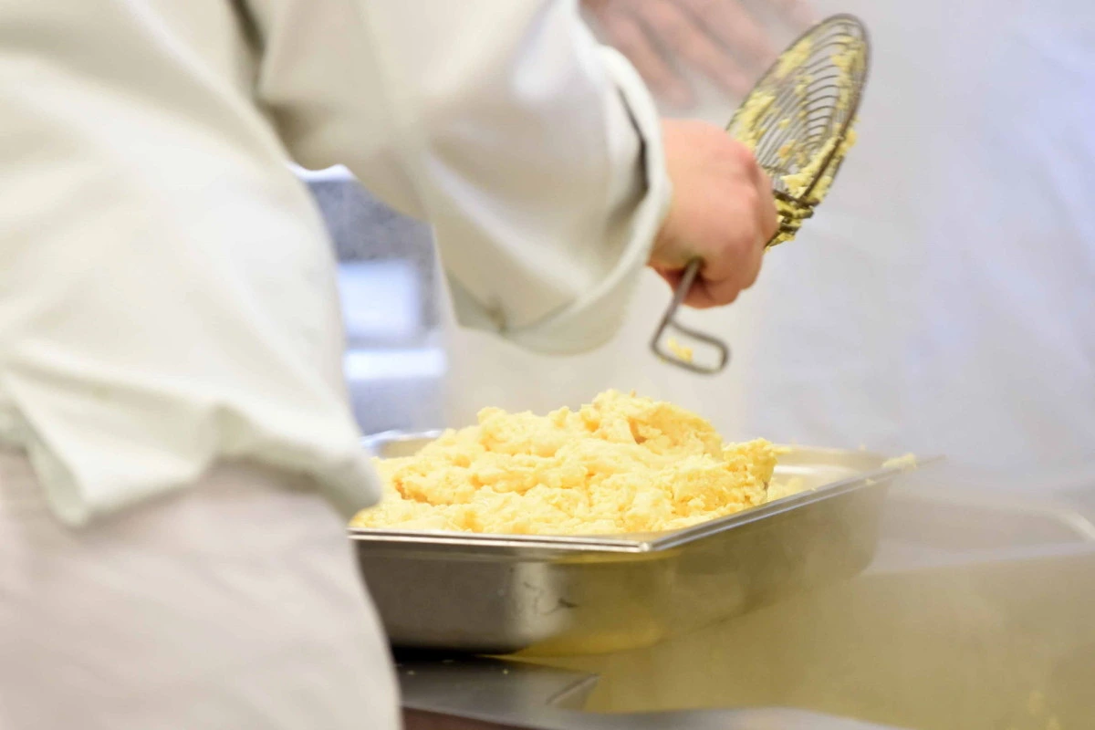 Koch verarbeitet Butter- oder Käsebruch im Edelstahlbehälter in einer Profiküche.