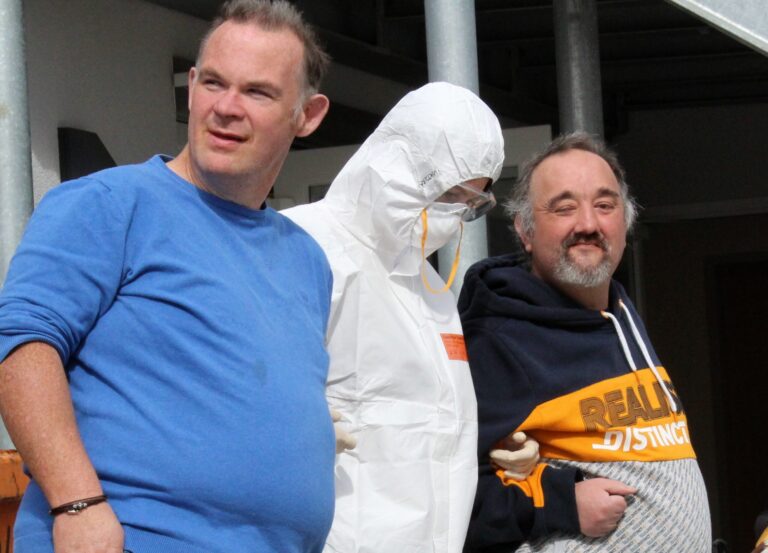 Teamfoto im Wohnheim Niederscheld: zwei Mitarbeiter neben Person im Corona-Schutzanzug