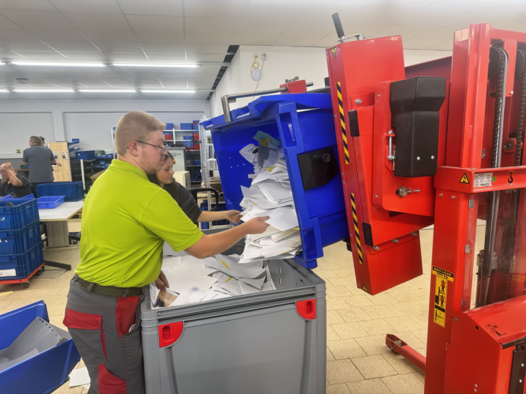 Mitarbeiter sortieren Papier in der Werkstatt mit Kippvorrichtung und Sammelbehälter.