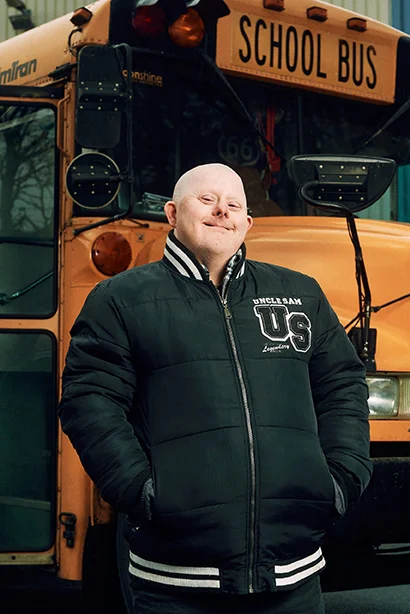 Mann in schwarzer Winterjacke steht vor gelbem amerikanischem Schulbus draußen.