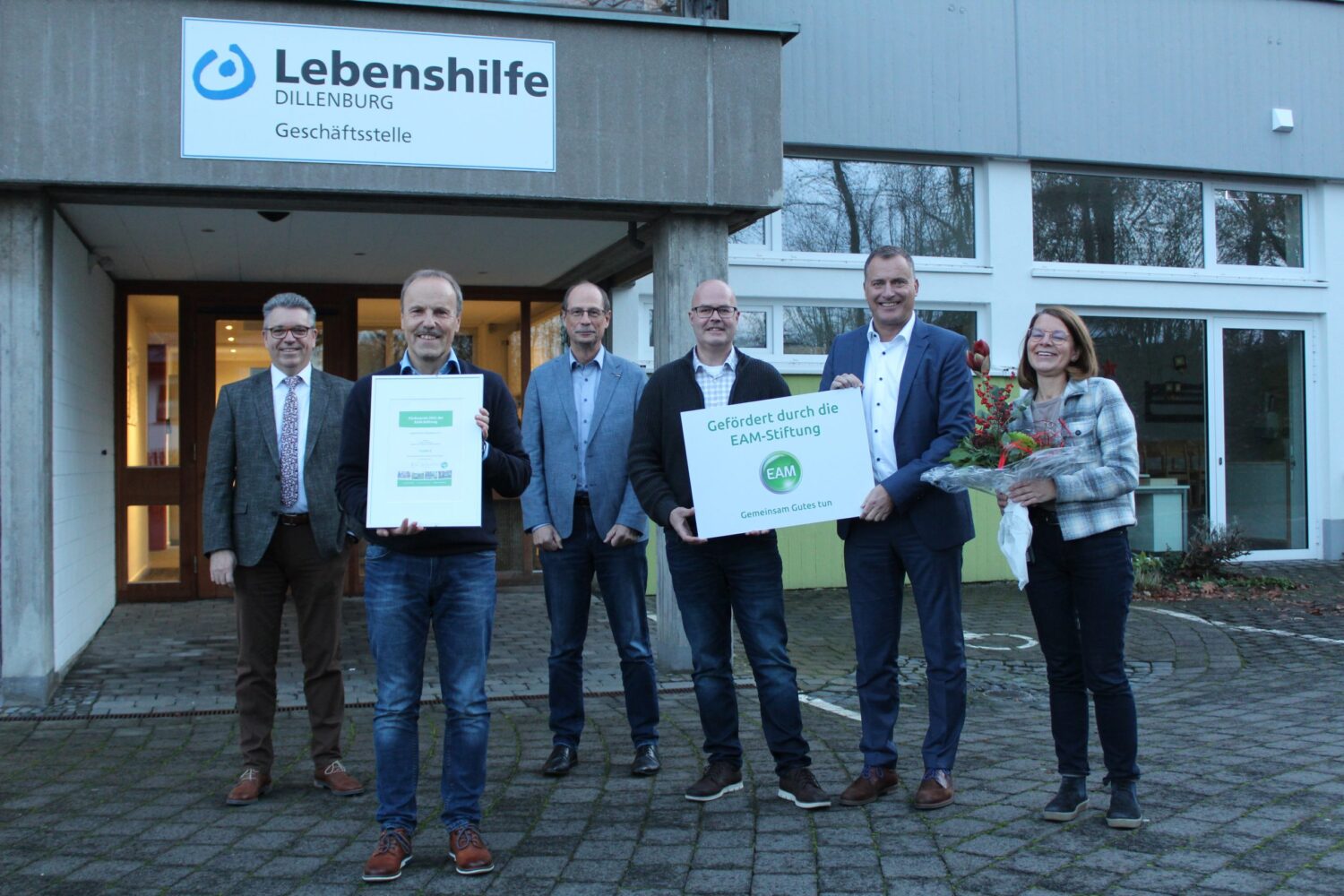 Gruppenfoto bei Lebenshilfe Dillenburg: Preisübergabe 10.000 Euro, EAM-Stiftung und Blumenstrauß.