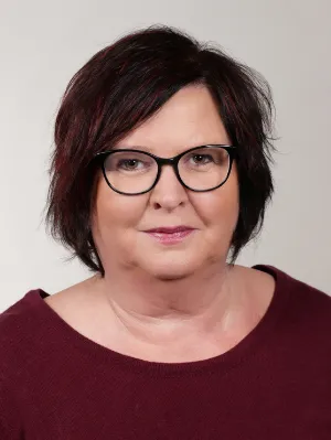 Professionelles Frauenporträt mit kurzem braunem Haar vor grauem Hintergrund, burgunderrotes Oberteil.