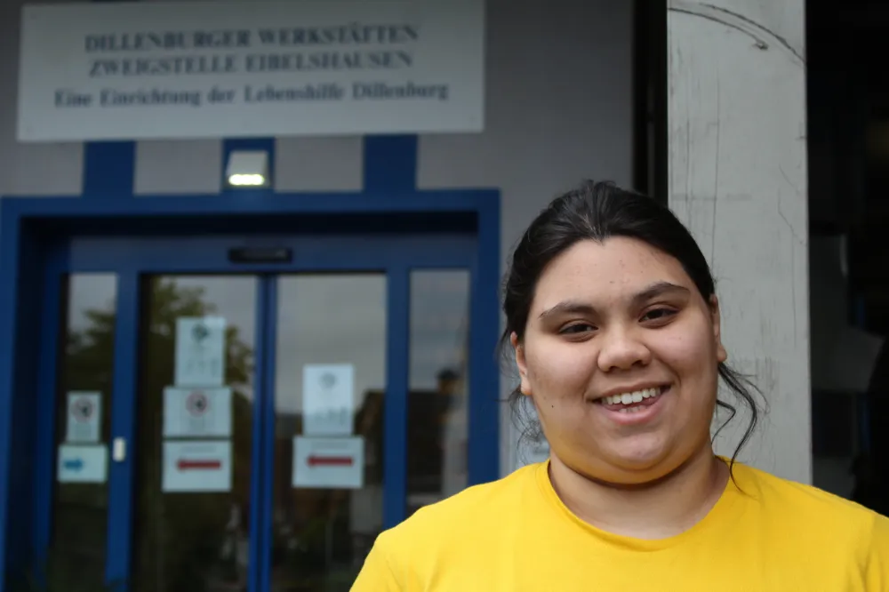 Lächelnde Mitarbeiterin vor dem Eingang der Dillenburger Werkstätten Eibelshausen, Lebenshilfe Dillenburg