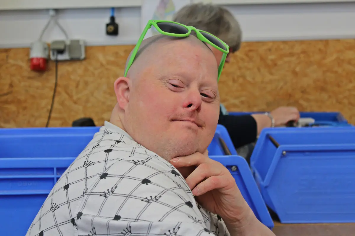 Lächelnder Mann im Workshop, grüne Sonnenbrille auf dem Kopf, blaue Boxen im Hintergrund.