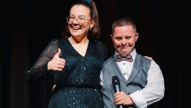 Moderationsduo Livia Warch und Jan Bernhardt lächeln auf der Bühne, Mikrofon und Daumen hoch.