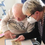 Pflegekraft zeigt Senior im Fotoalbum Erinnerungen am Tisch im Pflegeheim.