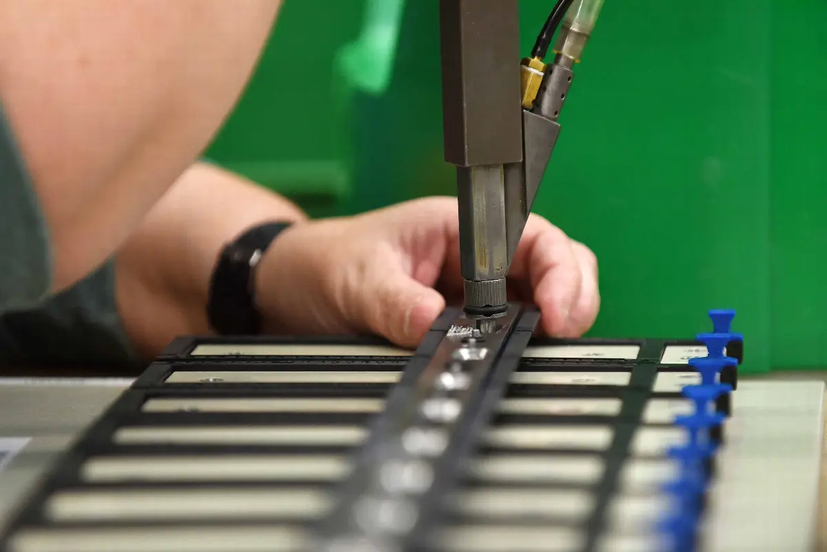 Mitarbeiter bedient Werkzeugmaschine bei Serienmontage schwarzer Bauteile in der Fertigungslinie.