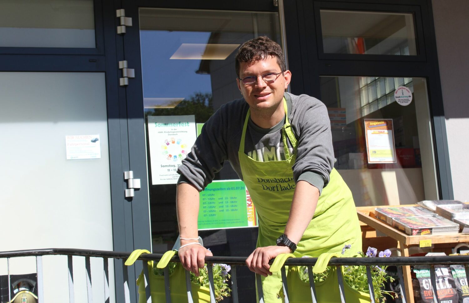 Simon Farago im Donsbacher Dorfladen, grüner Schürze, steht freundlich am Ladeneingang.