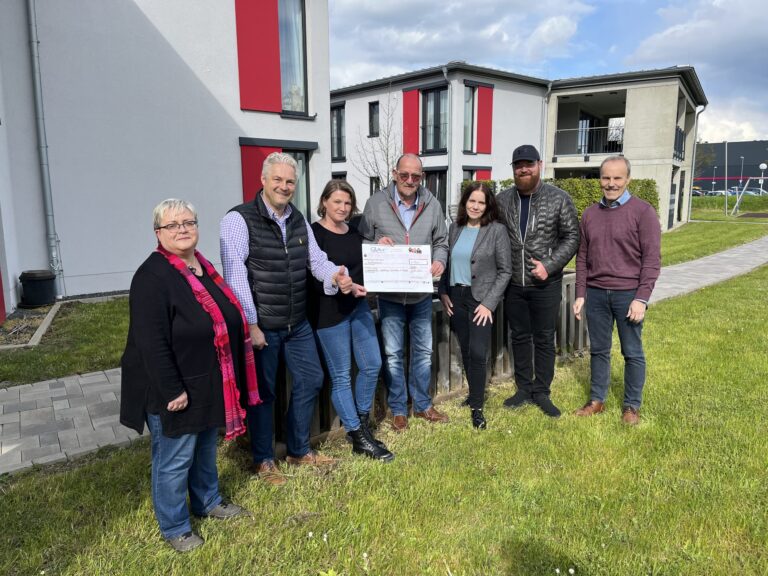 Team bei Spendenübergabe im Wohnhaus Haiger hält großen Scheck im Freien.