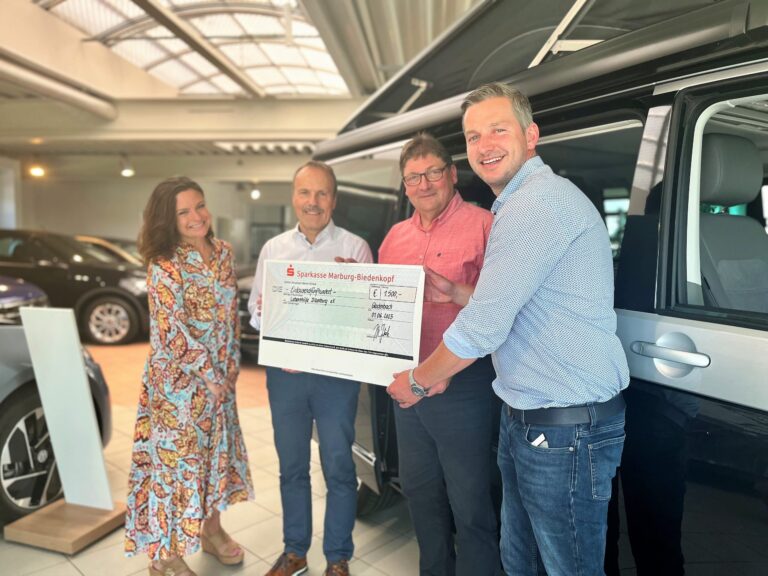 Vier Personen überreichen 2.500-Euro-Spendenscheck der Sparkasse Marburg-Biedenkopf im Autohaus.