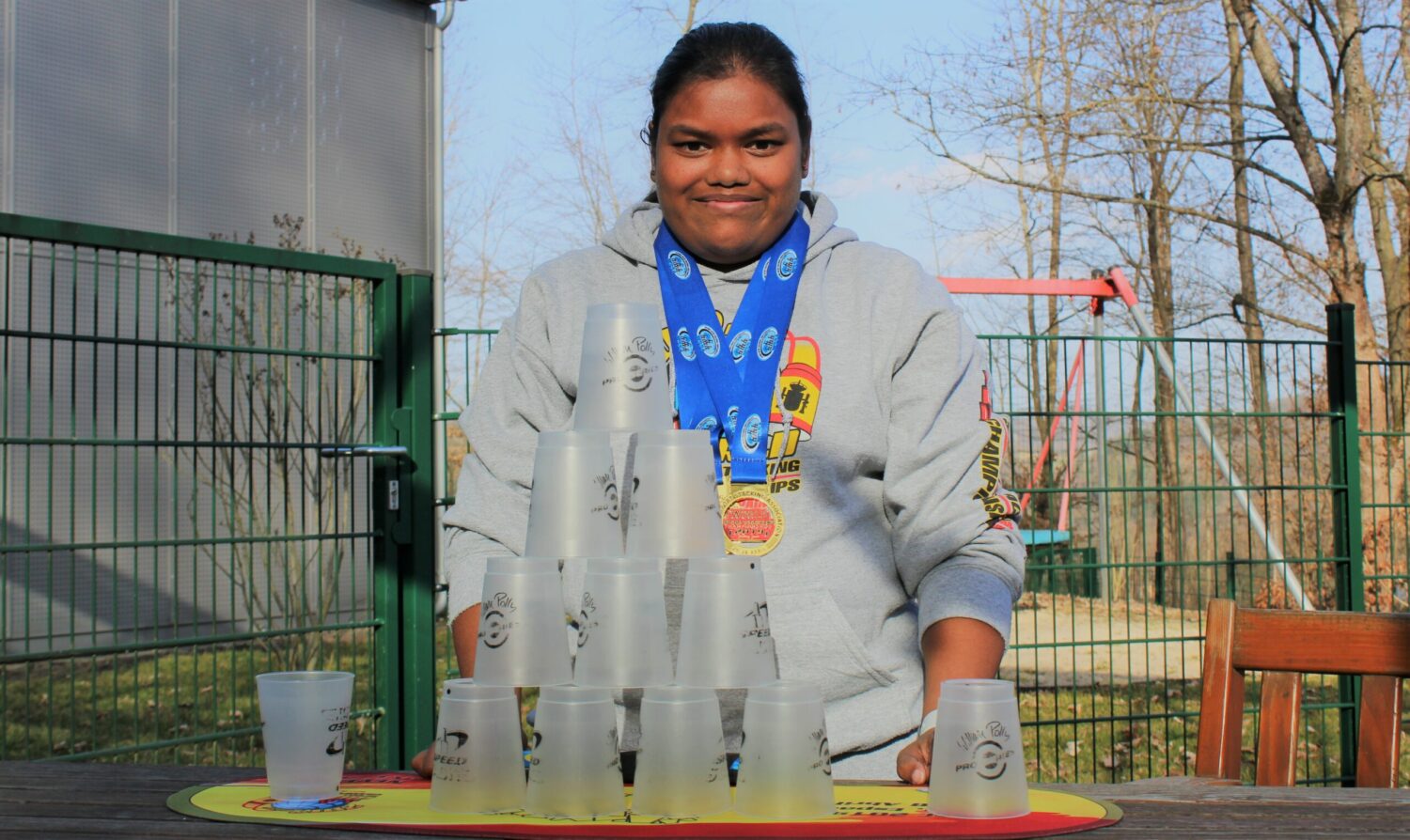 Weltmeisterin Stefanie Ammann mit Medaillen beim Sport-Stacking mit Bechern und Timer-Matte draußen.