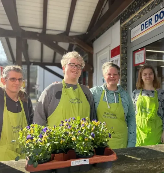 Team vom Dorfladen Nanzenbach mit grünen Schürzen am Eingang, Blumenverkauf im Dorfshop.