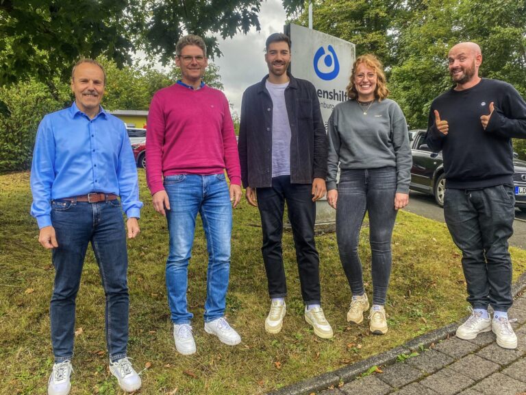 Teamfoto zur Kooperation Mosja und Lebenshilfe Dillenburg vor Firmenschild im Freien.