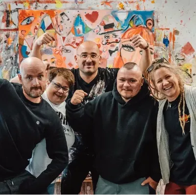 Kreatives Teamfoto im Kunststudio vor abstraktem Wandgemälde, lachende Künstlergruppe.