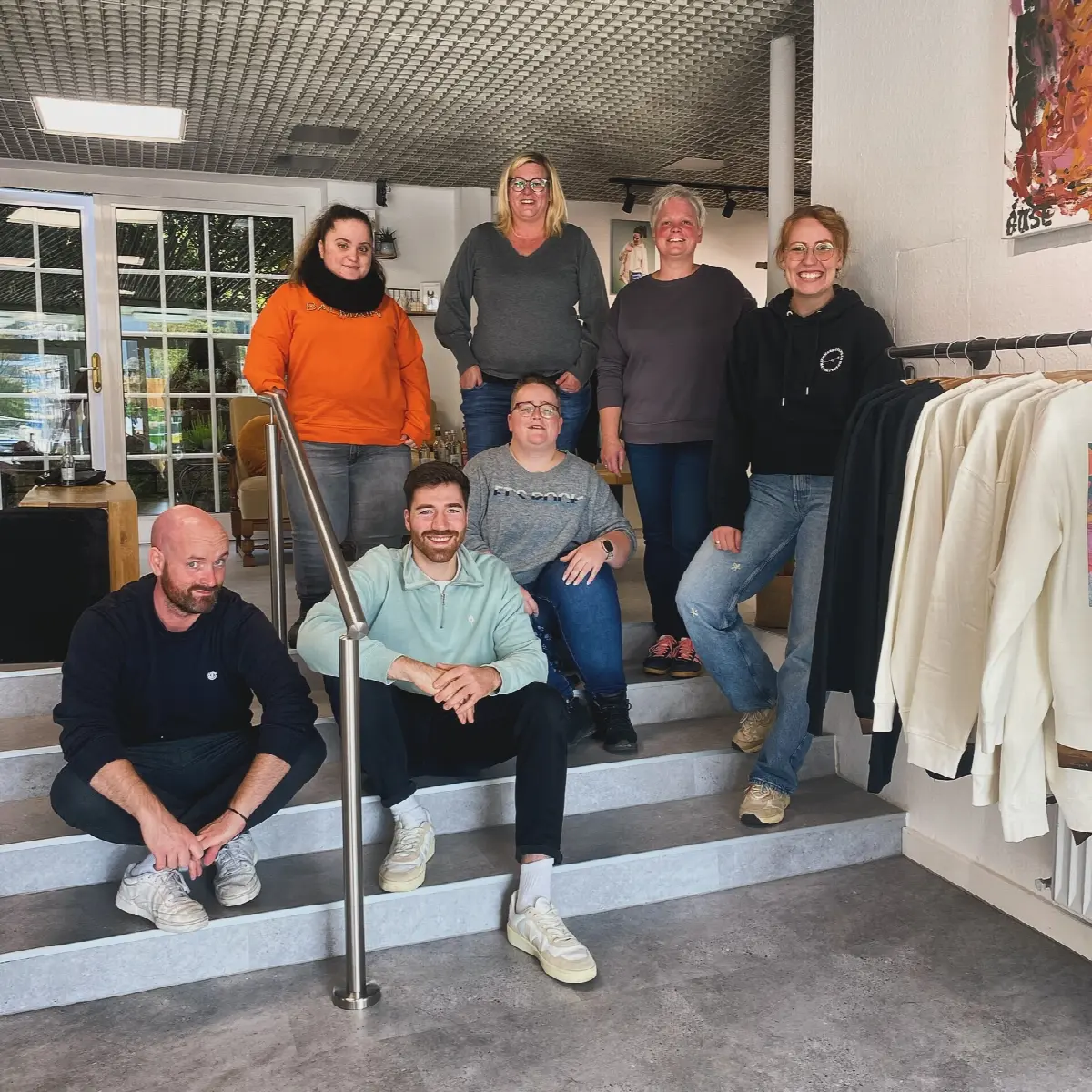 Teamfoto im Modeatelier und Showroom, Praktikumsteam lächelt zwischen Kleiderstangen.