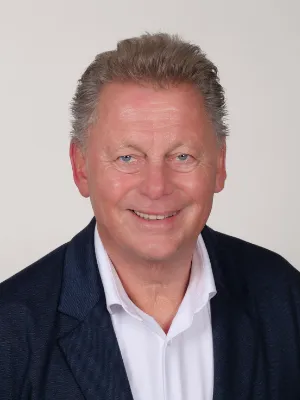 Freundliches Business-Porträt von Uwe Rompf im blauen Blazer vor hellem Hintergrund.