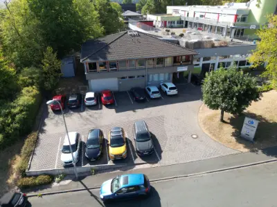 Drohnenaufnahme Verwaltungsgebäude mit Parkplatz, geparkten Autos und Zufahrt, modernes Büroensemble.