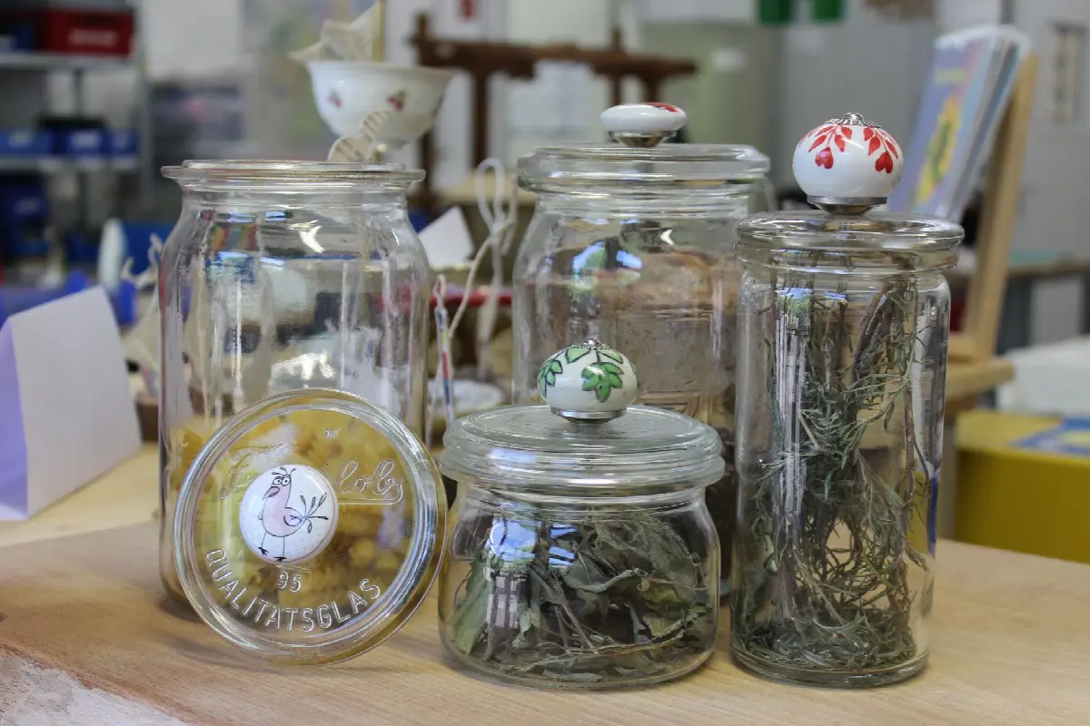 Vintage Glasgläser mit getrockneten Kräutern und handbemalten Blumen-Deckeln auf Holztisch