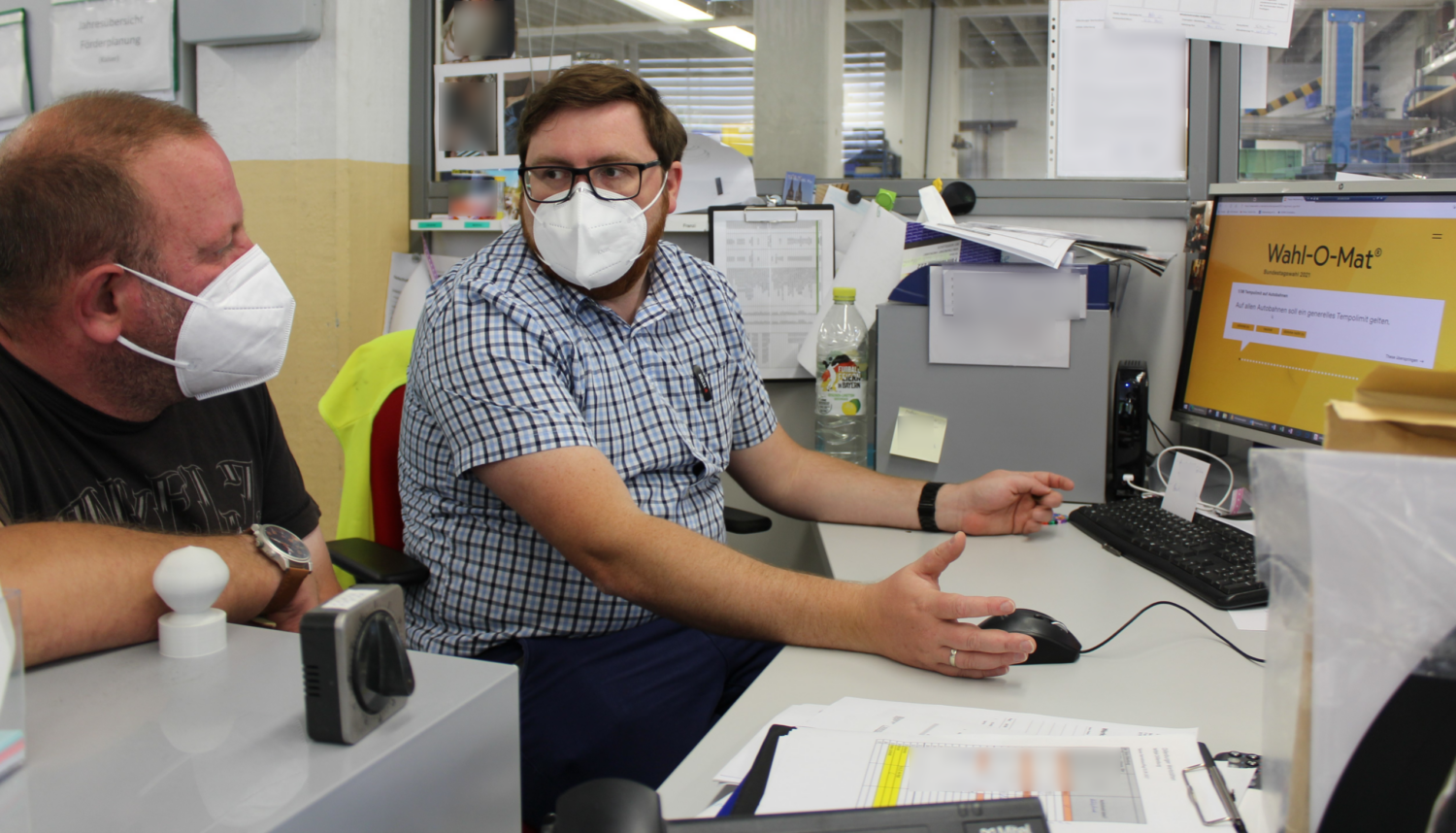 Zwei Kollegen mit Maske nutzen den Wahl-O-Mat am Arbeitsplatz im Büro.