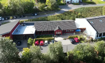 Luftaufnahme Reha-Werkstatt Gebäude mit Parkplatz und Autos in grüner Umgebung.