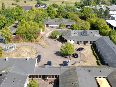 Luftaufnahme Wohnhaus Manderbach, Gebäudekomplex mit Innenhof, Parkplätzen und Bäumen im Grünen.