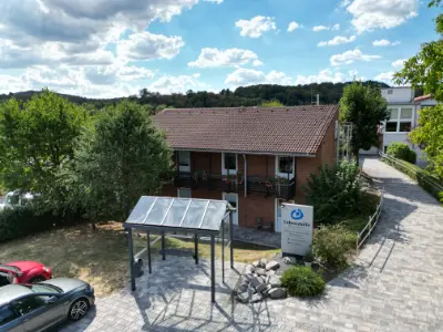 Backsteinhaus in Niederscheld mit Parkplatz, Grünanlage und blauem Himmel.